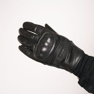 Angled view of the back of the leather glove, clearly displaying the integrated hard shell knuckle protection and the perforated leather panels on the wrist.