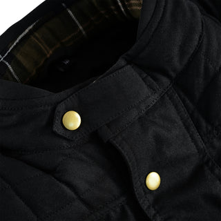 Extreme close-up of the black jacket's stand collar, focusing on the two large, round gold-colored snap buttons and the hidden tartan plaid interior lining.