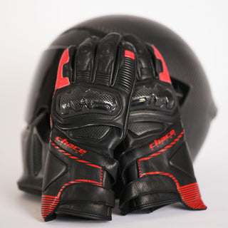 A pair of black and red leather Terra racing gloves with carbon fiber knuckle protection resting on a dark motorcycle helmet, showcasing the palm-up view.