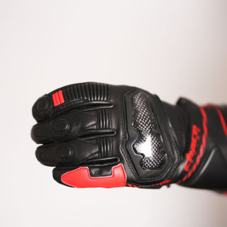 Close-up of the back of the Terra racing glove, highlighting the glossy, black carbon fiber knuckle protector, accordion stretch paneling, and red textile accents.