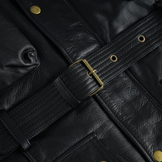 Extreme close-up of the jacket's leather waist belt, showing the stitched detailing, the adjustment holes, and the antique brass buckle and loop keeper.