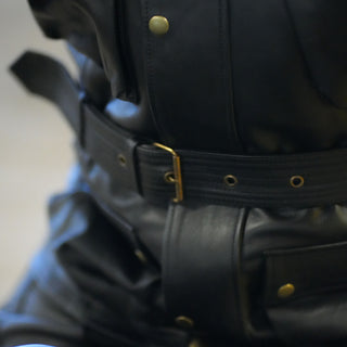 Close-up of the rider's waist, showing the wide black leather waist belt cinched by a gold/brass buckle, with punched adjustment holes visible.