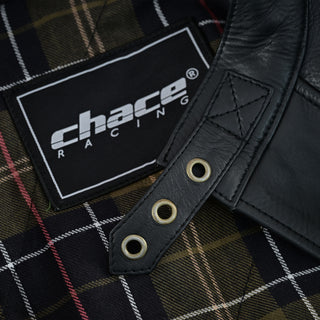 Close-up of the jacket's collar area, showing the leather throat latch strap with brass eyelets against the tartan plaid interior lining and the Chace Racing brand tag.