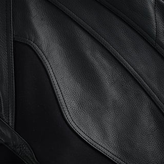 Close-up showing two curved panels of black leather stitched together, with a black textile stretch fabric insert visible between them, designed for flexibility.