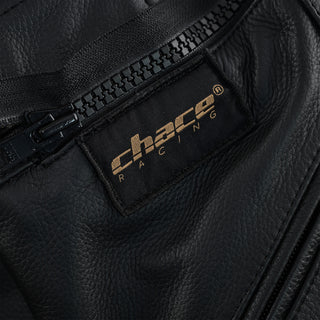 Close-up of the trousers' fly area, showing the black zipper and the black and gold stitched "Chace Racing" brand patch on the leather.