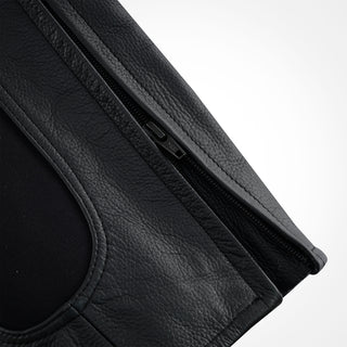 Close-up of the lower section of the leather trousers, showing the zippered closure for fitting over a boot and the visible black stretch textile panel adjacent to the zipper.