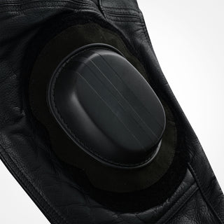 Close-up of the black knee slider pad, showing embossed horizontal grooves on its surface and the surrounding black leather and Velcro base material.