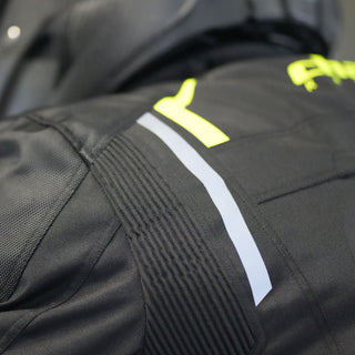 Close-up of the jacket's shoulder on a rider, highlighting the accordion stretch panel for mobility, a vertical silver reflective stripe, and a hi-vis yellow accent panel.