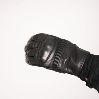 Side view of the glove being worn and flexed, clearly showing the profile of the hard knuckle protector, the short cuff wrist, and perforated leather detailing.