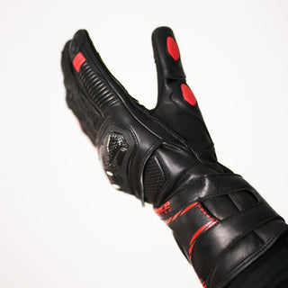 Side view of the glove being worn, highlighting the carbon fiber knuckle protector, the red thumb accent, and the reinforced wrist/gauntlet area.
