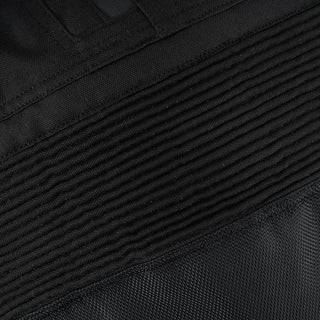 Extreme close-up of the black textile material, highlighting the ribbed, finely stitched accordion stretch panel above the knee for riding mobility.