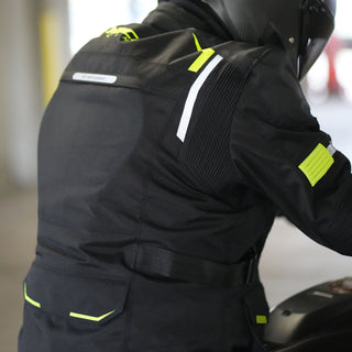 Rear three-quarter view of a rider on a motorcycle wearing the black jacket, showing the back 'Air Vent System' flap, the hi-vis yellow accents, and the adjustable waist belt.