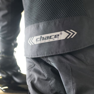 Extreme close-up of the lower back hem of the black motorcycle jacket, highlighting the large, reflective strip with the "Chace Racing" logo and arrow graphics for high visibility.
