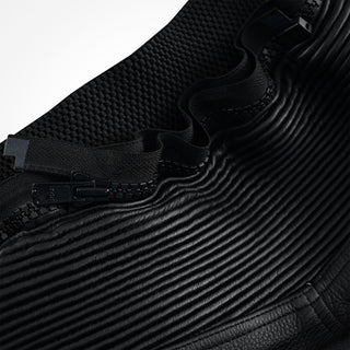 Close-up of the black leather trousers showing a heavy-duty zipper and pull tab interfacing with both the accordion stretch leather panel and a separate knit stretch fabric.